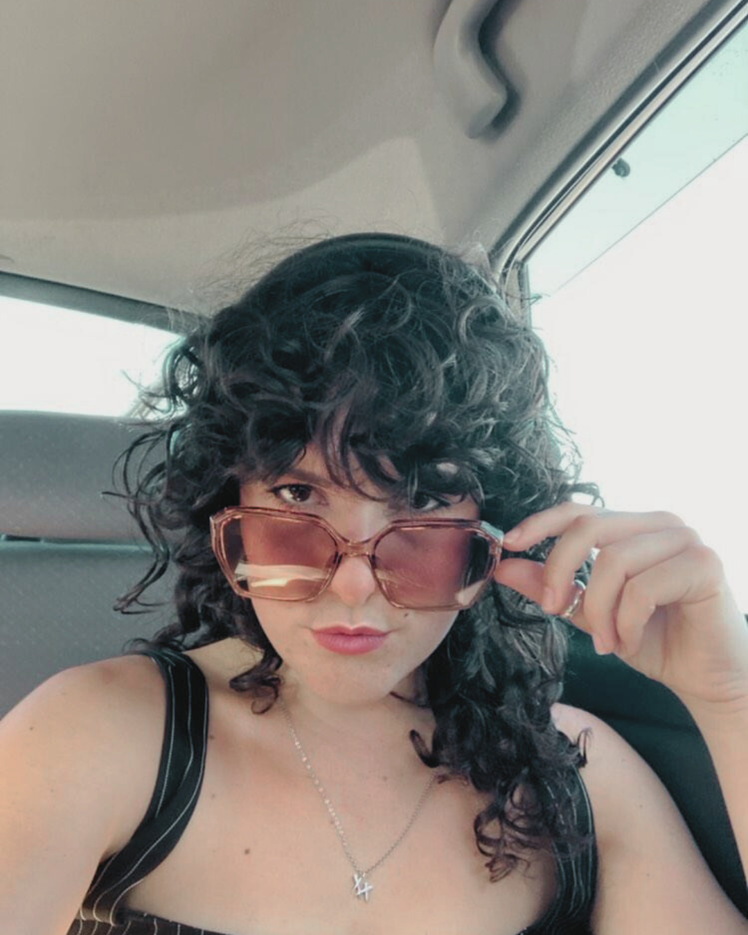 Person with curly hair wearing sunglasses inside a vehicle