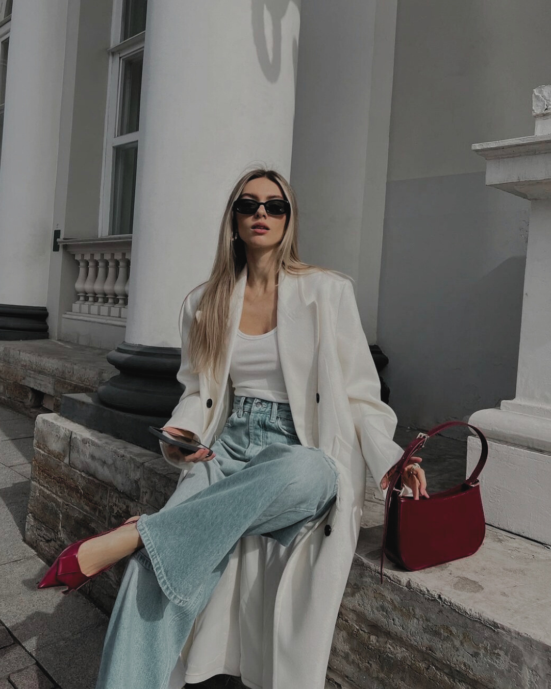 Woman in stylish outfit sitting on steps outdoors with a red handbag.