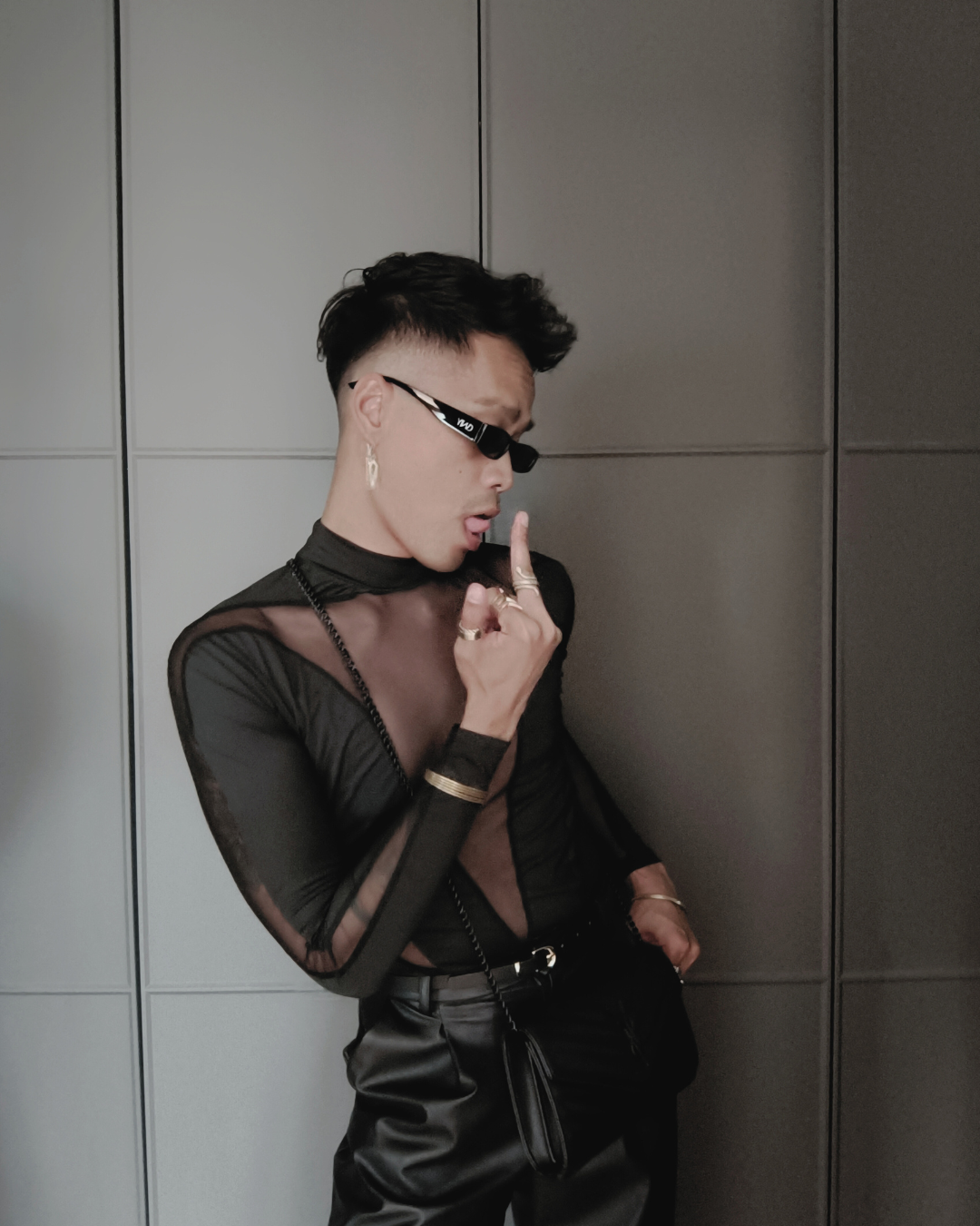 Person wearing a black outfit with sheer details against a gray wall